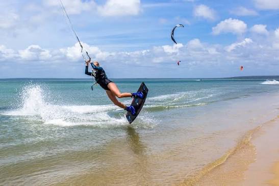 Kitesurfer carving through the shallows, kites in the sky behind